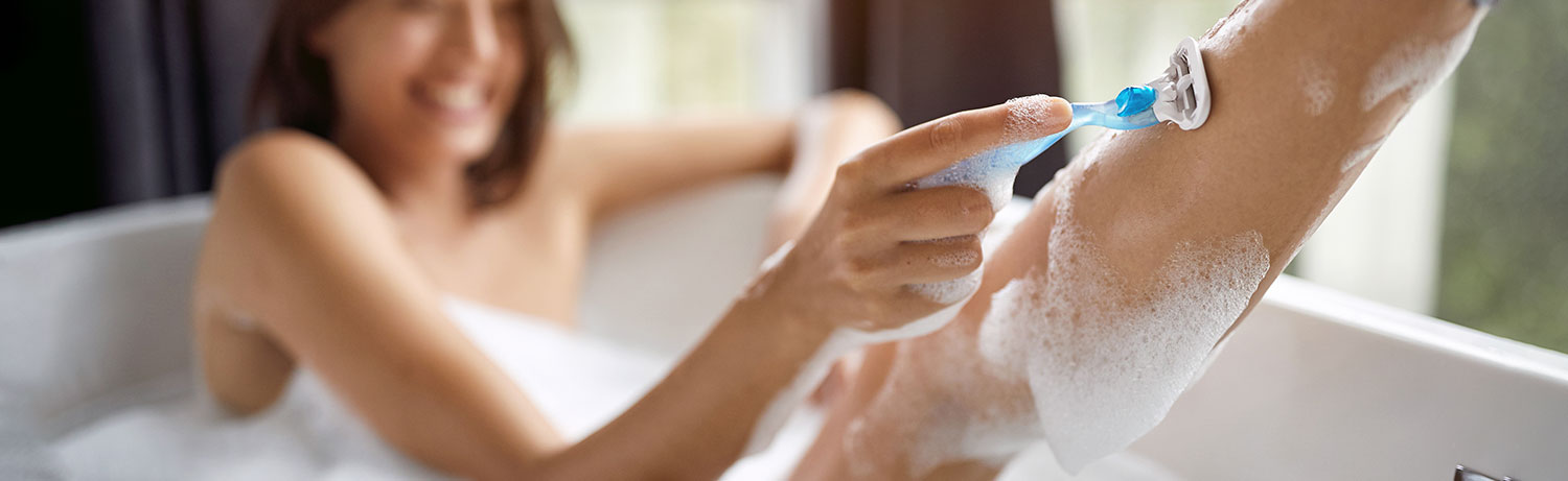 Frau rasiert sich die Beine in der Badewanne